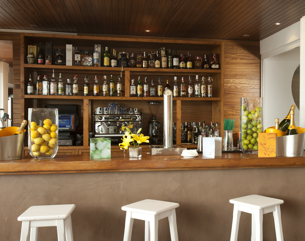 Barra del bar con botellas, taburetes blancos y cubitera