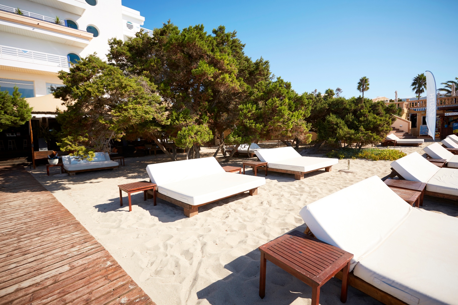 Daybeds de madera y tumbonas sobre la arena junto al edificio del hotel